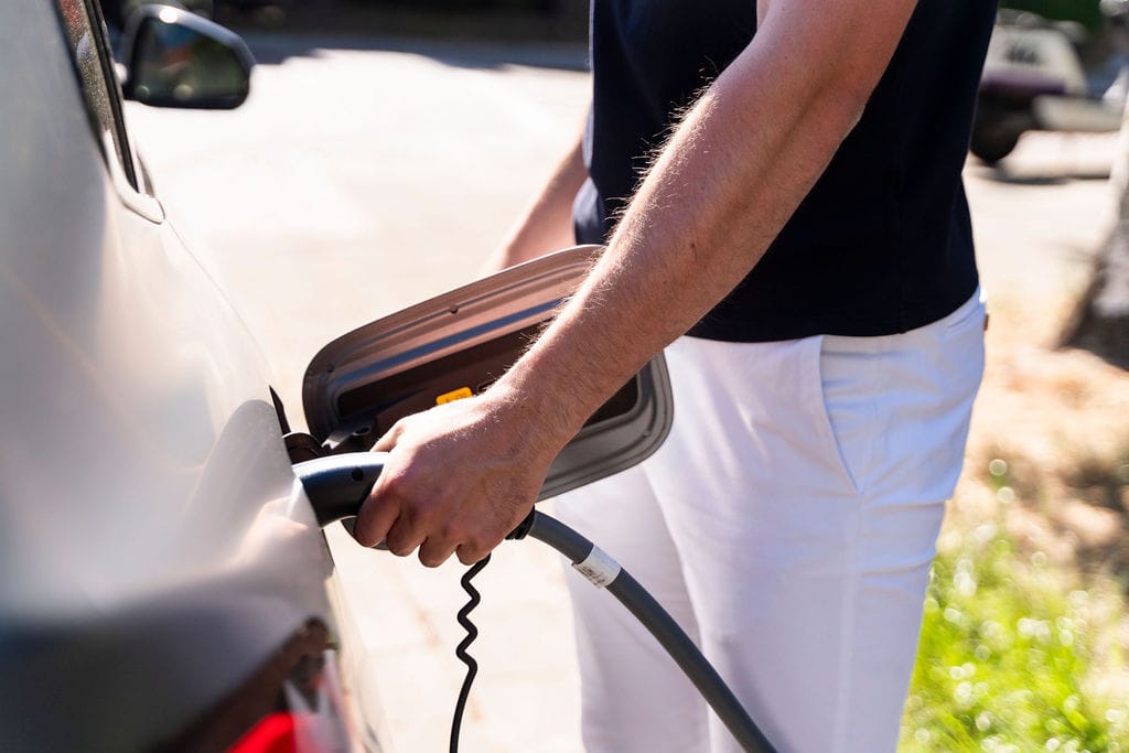Elektisch auto laden man met witte broek en stekker in auto